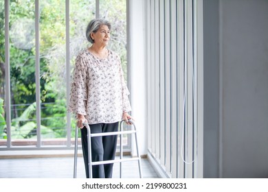 Asian elderly woman using a cane to help her walk near glass window in home, medical care and life insurance concepts.