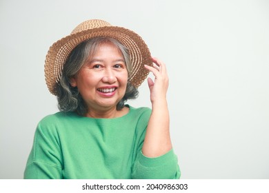 Asian Elderly Woman Wearing A Green Shirt And A Hat She Smiles Happily, Getting Dressed For A Trip. Standing On A White Background. Travel Concept Elderly People Are Happy In Retirement.