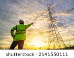 Asian electrical engineer standing and watching at the electric power station to view the planning work by producing electricity at high voltage electricity poles.