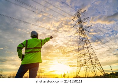Asian electrical engineer standing and watching at the electric power station to view the planning work by producing electricity at high voltage electricity poles.