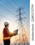 Asian electrical engineers checking location using a notebook computer standing at a power station to view the planning work by producing electrical energy at high voltage electrodes. Vertical image.