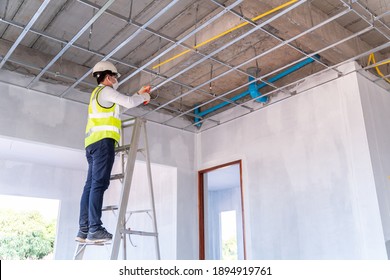 Asian electrician wearing a mask installing laying electrical cables on the ceiling with pliers inside the house under construction.