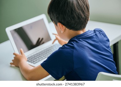 Asian elementary school boy using laptop for online learning (back view)