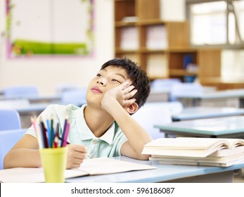 asian elementary schoolboy thinking while doing homework in classroom, looking up hand on cheek. - Powered by Shutterstock