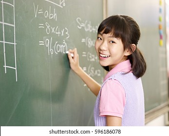 asian elementary schoolgirl looking at camera smiling while solving a math problem. - Powered by Shutterstock