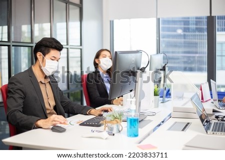 Asian employees wearing medical mask working on computer at desk in the office