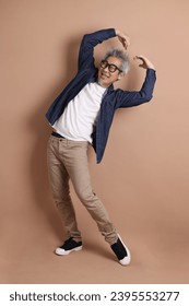 Asian energetic senior man with glasses posing  isolated on the brown background with casual clothes. mature man, Asian man. Elderly,  studio shot. Multiple emotions. - Shutterstock ID 2395553277