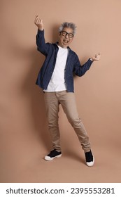 Asian energetic senior man with glasses posing  isolated on the brown background with casual clothes. mature man, Asian man. Elderly,  studio shot. Multiple emotions. - Shutterstock ID 2395553281