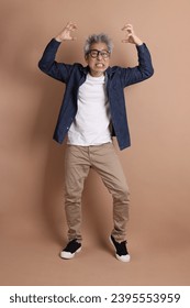 Asian energetic senior man with glasses posing  isolated on the brown background with casual clothes. mature man, Asian man. Elderly,  studio shot. Multiple emotions. - Shutterstock ID 2395553959