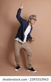Asian energetic senior man with glasses posing  isolated on the brown background with casual clothes. mature man, Asian man. Elderly,  studio shot. Multiple emotions. - Shutterstock ID 2395553963