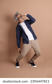 Asian energetic senior man with glasses posing  isolated on the brown background with casual clothes. mature man, Asian man. Elderly,  studio shot. Multiple emotions. - Shutterstock ID 2396447811