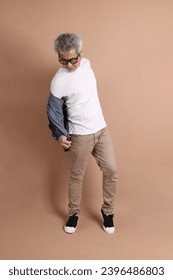 Asian energetic senior man with glasses posing  isolated on the brown background with casual clothes. mature man, Asian man. Elderly,  studio shot. Multiple emotions. - Shutterstock ID 2396486803