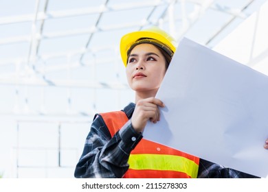 Asian engineer architect worker woman holding blueprint infrastructure progress at construction site, engineering female leader standing hold paper plan control worker to building project