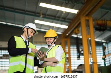 Asian Engineer Factory  And Female Workers  With Safety Helmet Hat Using Digital Tablet Check Product Quality Of Industrial Machine. Manufacturing Industry To Produce Car Parts. Quality Assurance (QA)