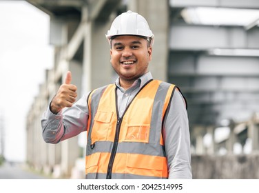 Asian engineer handsome man or architect looking construction with white safety helmet in construction site. Standing at highway concrete road site Showing thumbs up.