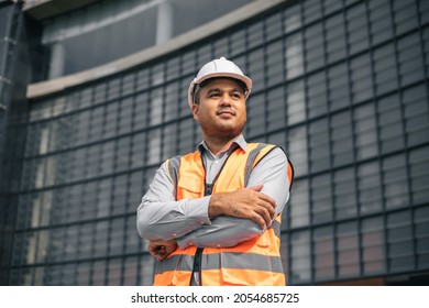 Ingeniero asiático hombre o arquitecto apuesto mirando hacia adelante con casco blanco de seguridad en el sitio de construcción. Parado en una construcción moderna. Construcción de proyectos de trabajo de trabajadores asiáticos