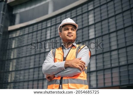 Asian engineer handsome man or architect looking forward with white safety helmet in construction site. Standing at modern building construction. Worker asian man working project building