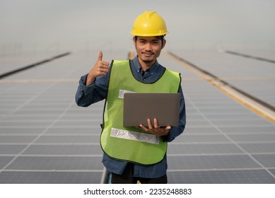 Asian Engineer with laptop in hand standing on factory roof with solar panels - Shutterstock ID 2235248883