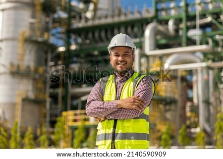Asian engineer man with white safety helmet standing front of oil refinery. Industry zone gas petrochemical. Factory oil storage tank and pipeline. Workers work in the refinery construction building