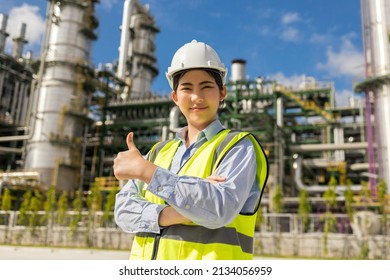 Asian engineer manager woman with white safety helmet standing front of oil refinery. Industry zone gas petrochemical. Factory oil storage tank and pipeline. Workers in the refinery construction.