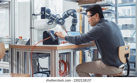 Asian Engineer Moving Robotic Arm With Control Panel And Developing Program On Laptop. Robotics Specialist Designs Plans And Processes Needed To Build Robots. Computer Science Laboratory.