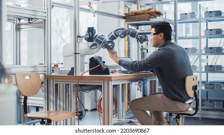 Asian Engineer Moving Robotic Arm With Control Panel While Developing Program On Laptop. Robotics Specialist Designs Plans And Processes Needed To Build Robots. Computer Science Laboratory.