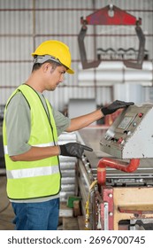 Asian engineer operating a touch screen control panel of a roll forming machine, managing metal sheet production in a modern industrial factory.