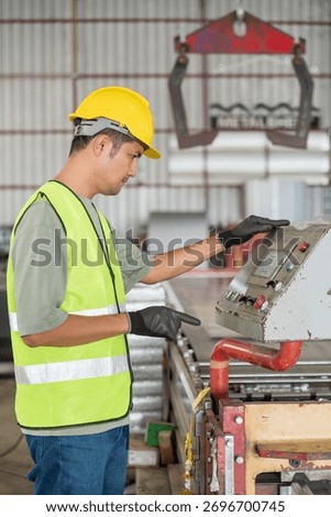 Asian engineer operating a touch screen control panel of a roll forming machine, managing metal sheet production in a modern industrial factory.
