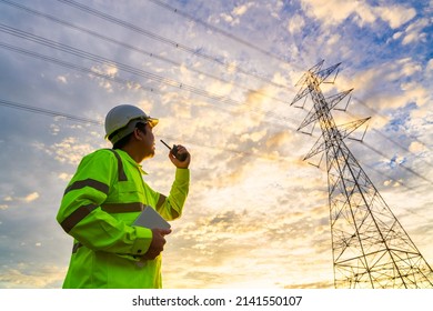 Asian engineer use radio checks at a power station for planning work by generating electricity from a high-voltage transmission tower at sunset.
