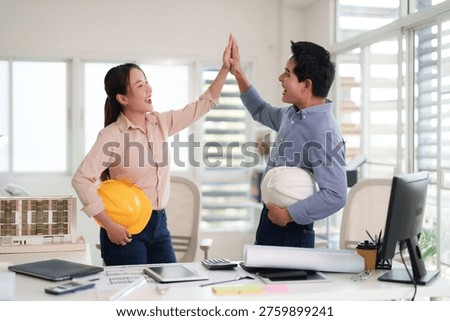 Asian engineering professionals high five celebrating project success showing teamwork. Architects in modern office expressing achievement.