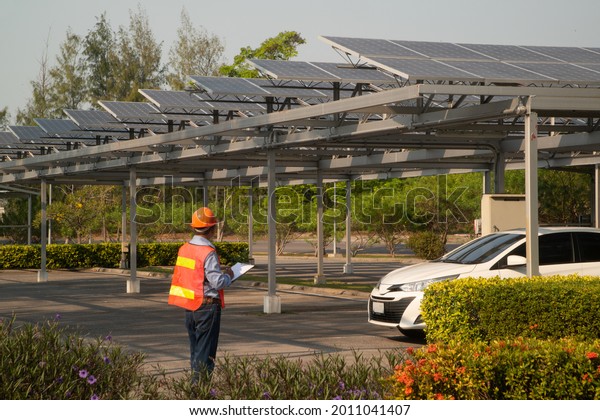Asian engineers inspecting solar panels mounted on\
roofs of car parks which is the most efficient use due to limited\
space.