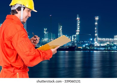 Asian Engineers Thinking And Holding The Note Pad On Oil And Gas Refinery Or Petrochemical Factory At Twilight Time, Industrial Concept