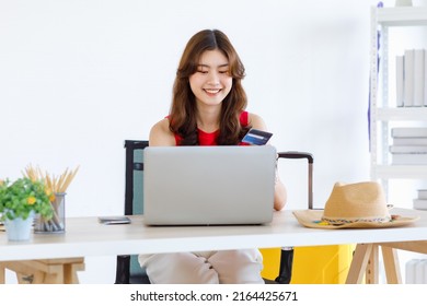 Asian Excited Happy Female Traveler In Casual Outfit Sitting Looking At Laptop Computer Holding Fists Up Celebrating After Lucky Winning Free Travelling Trip Vacation Holiday Package Prize Online.