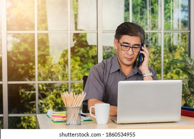 Asian Executive Senior Businessman Sitting On Desk Office He Using His Mobile Phone And Talking With Somebody, The Confident Middle Aged Handsome Man Using Laptop Computer At Workplace Home Office