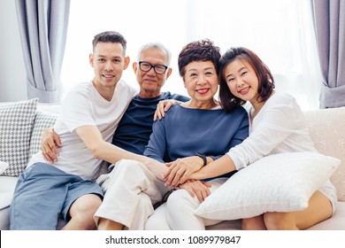 Asian family with adult children and senior parents relaxing on a sofa at home together