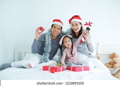 Asian Family Celebrating Christmas Wearing Red Santa Claus Hat With Decorative Gifts And Gift Boxes Or Present In Bedroom, Holiday In Festive Merry Christmas Or X'mas And Happy New Year Concept