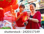 Asian family celebration Chinese Lunar New Year festival together. Mother and daughter choosing and buying home decorative ornaments and joss paper celebrating Chinese New Year at Chinatown market.