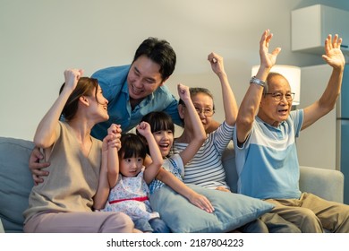 Asian family cheering and watching football on television at home.  Muti-generation, Senior old couple and young parents sit on sofa with little children looking at tv and feeling happy in living room - Shutterstock ID 2187804223