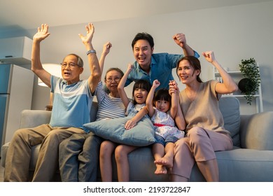 Asian family cheering and watching football on television at home. Muti-generation, Senior old couple and young parents sit on sofa with little children looking at tv and feeling happy in living room - Powered by Shutterstock