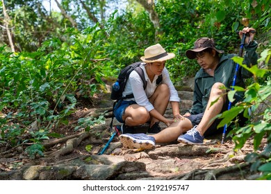 Asian Family Couple On Summer Holiday Vacation. Mature Adult Couple Hiking Together In Forest. Senior Man Injured On Knee During Trekking With His Wife. Adventure Travel And Health Care Concept.