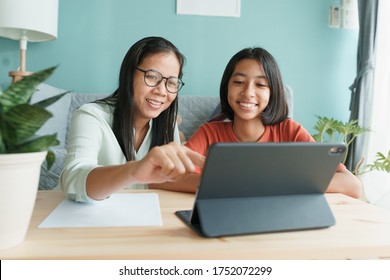 Asian family with a daughter do homework by using tablet with mother help. Happy smile Asia kid while sitting in the living room at home morning. Concept of online learning at home