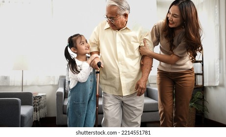 Asian Family, Daughter And Granddaughter Take Care Support Senior Mature Grandfather Who Is Suffering From Knee Pain Walking Outside To Take A Walk And Grandpa With A Stick, Elderly Health Care