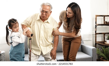 Asian Family, Daughter And Granddaughter Take Care Support Senior Mature Grandfather Who Is Suffering From Knee Pain Walking Outside To Take A Walk And Grandpa With A Stick, Elderly Health Care