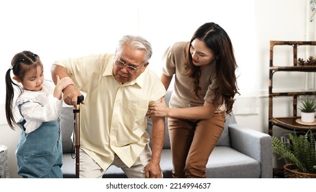 Asian Family, Daughter And Granddaughter Take Care Support Senior Mature Grandfather Who Is Suffering From Knee Pain Walking Outside To Take A Walk And Grandpa With A Stick, Elderly Health Care