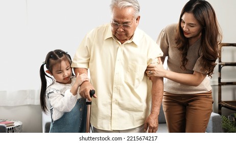 Asian Family, Daughter And Granddaughter Take Care Support Senior Mature Grandfather Who Is Suffering From Knee Pain Walking Outside To Take A Walk And Grandpa With A Stick, Elderly Health Care