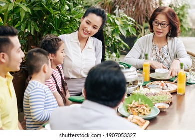 Asian Family Eating Traditional Dishes And Talking At Dinner Table Outdoors