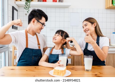 Asian  family enjoying breakfast at cozy kitchen, little girl daughter sitting on table, drinking milk with smiling father and mother in morning. Happy family in kitchen. - Powered by Shutterstock