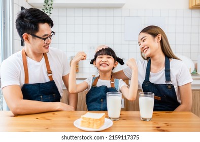 Asian  family enjoying breakfast at cozy kitchen, little girl daughter sitting on table, drinking milk with smiling father and mother in morning. Happy family in kitchen. - Powered by Shutterstock