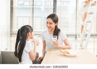 Asian  Family Enjoying Breakfast At Living Room. Little Girl Daughter Sitting On Table, Drinking Milk With Smiling Father And Mother In Morning. Happy Family At Home.