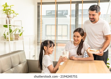 Asian  Family Enjoying Breakfast At Living Room. Little Girl Daughter Sitting On Table, Drinking Milk With Smiling Father And Mother In Morning. Happy Family At Home.